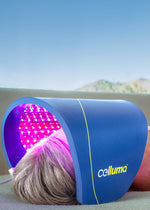 Woman lying on a couch at home under a Celluma LED light therapy device receiving a treatment for the reduction of fine lines and wrinkles. A pink glow emanates from the device that emits red, blue, and near-infrared wavelengths of light energy.