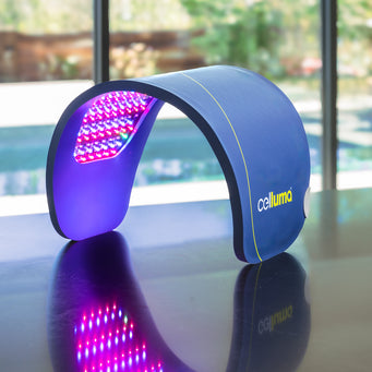 Close up of a large, single-panel Celluma LED light therapy device emitting a pink glow from the combined red and blue light energy in the anti-aging wrinkles mode. The device has been shaped into a C-curve, standing on it's own on top of a reflective countertop.